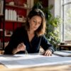 Een architect buigt zich thuis aan zijn bureau over bouwtekeningen en verdiept zich in verschillende bouwmethodes.