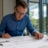 Man zit aan de eettafel thuis verdiept in bouwtekeningen
