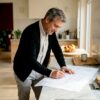 Een architect buigt zich over de verbouwingstekeningen aan zijn bureau.