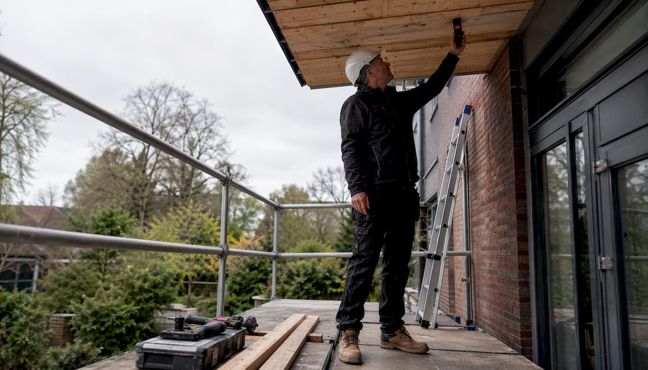 Een woningeigenaar controleert het dakbeschot op vocht met een vochtmeter.