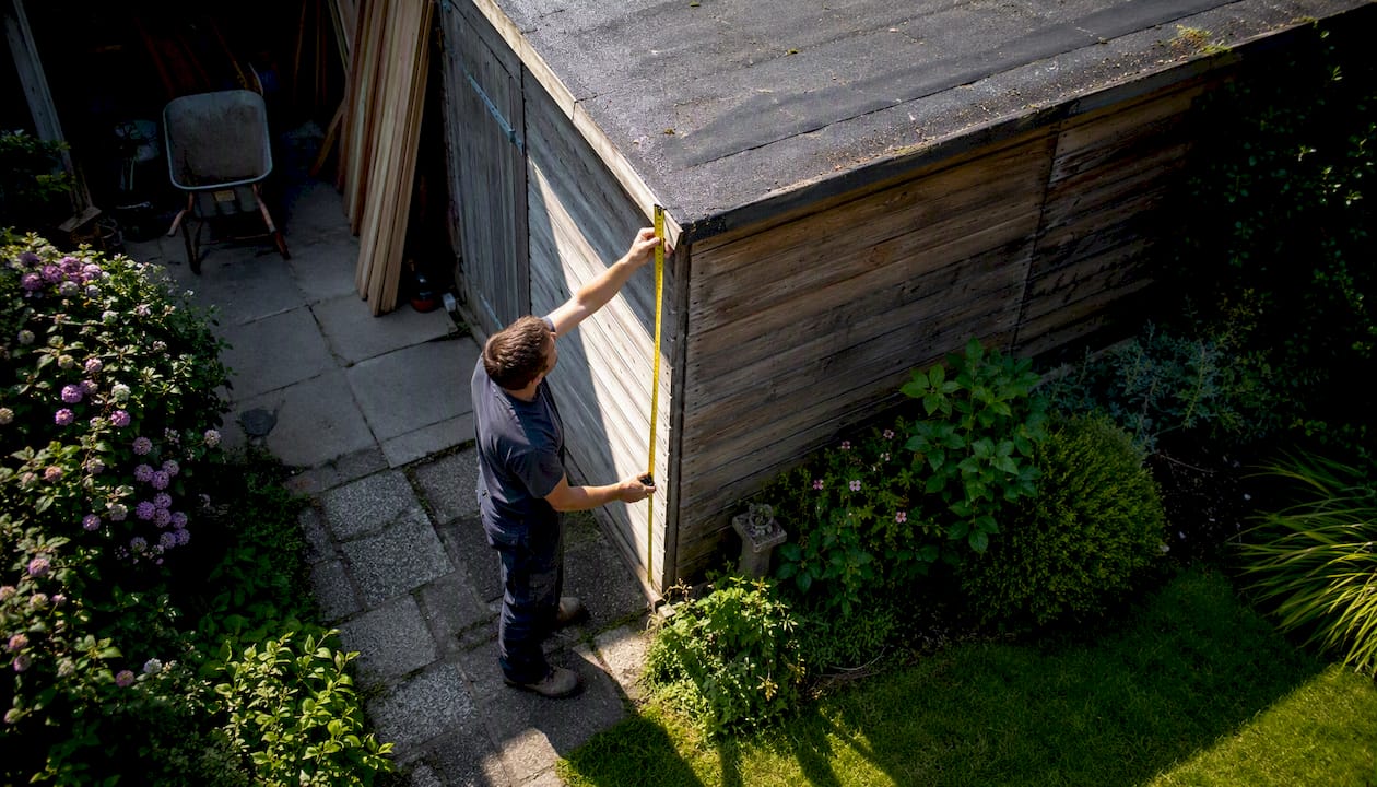 Een dakdekker neemt nauwkeurig de maten op van het tuinhuisje in de achtertuin.
