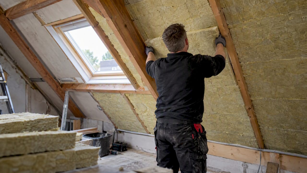 Dakdekker brengt isolatie aan tussen houten dakspanten