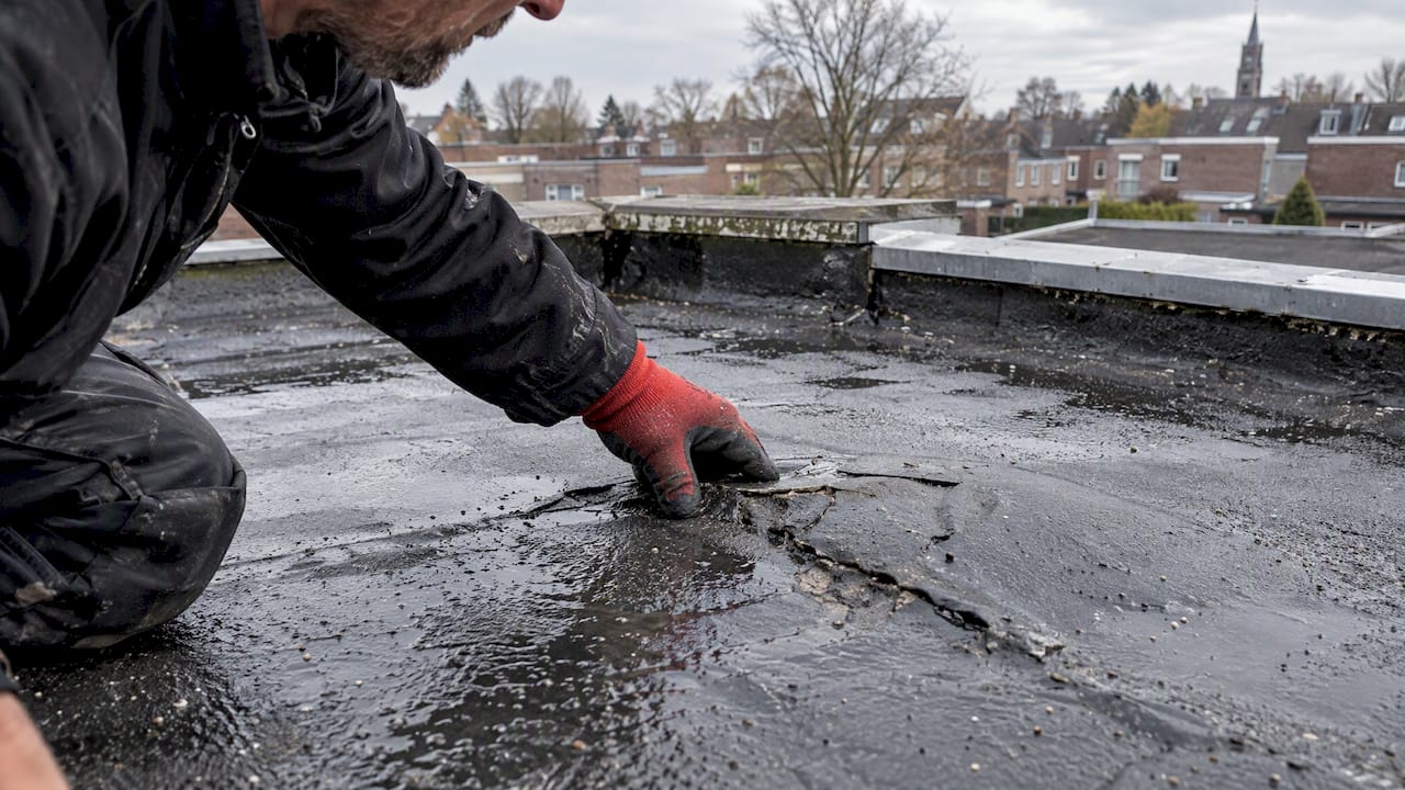 Dakdekker onderzoekt beschadigd bitumen op plat dak