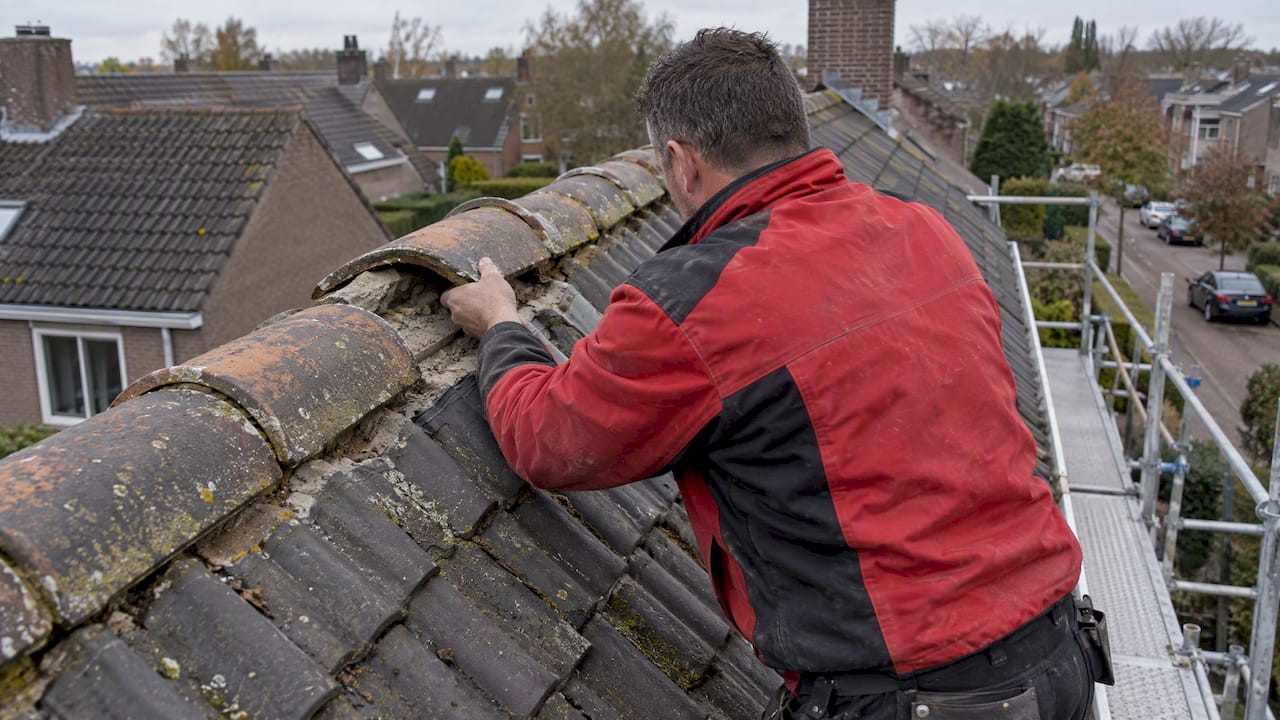 Een dakdekker repareert een nokvorst op een pannendak
